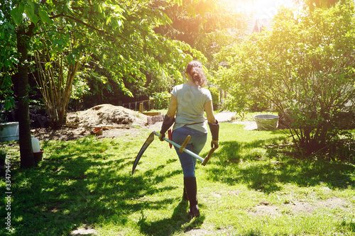 Woman at gardening in the garden mows wild meadow with scythe on a sunny summer day photo