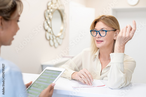 Fotografia, Obraz Content mature lady in glasses standing at beauty salon counter and asking admin
