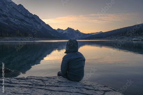 Man traveler sitting on rock in Medicine Lake in the morning at Jasper national park