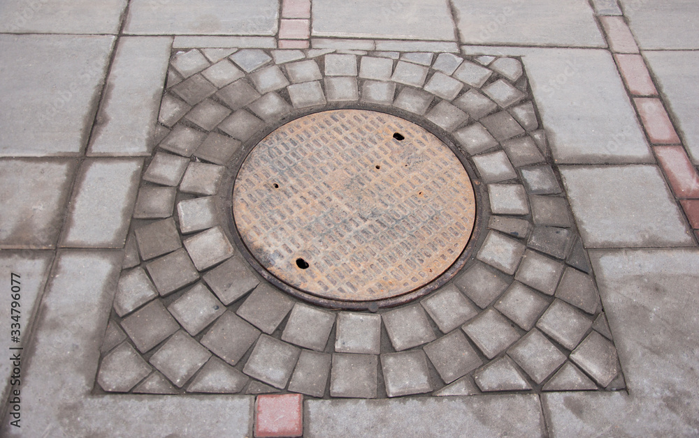 rustproof manhole cover on the background of paving tiles, urban networks rustproof manhole cover on the background of paving tiles, urban networks