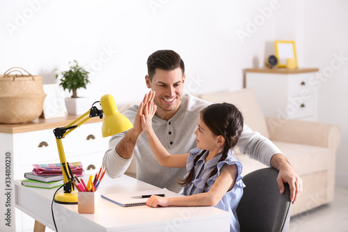 Father and daughter doing homework together at table indoors photo