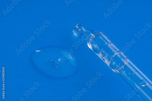Cosmetic pipette with serum smear smudge drop swatch of collagen and peptides closeup isolated on blue. Liquid dropper with hyaluronic acid, peeling with bubbles. Anti aging woman beauty face product. © photo-lime