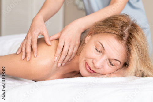 Relaxed mature woman lying with closed eyes on massage table and enjoying manual massage in spa salon