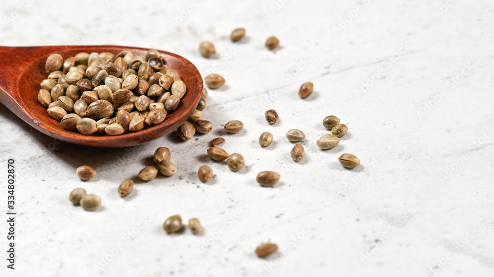 Unpeeled hemp - Cannabis sativa - in small dark wooden spoon on white stone board desk Unpeeled hemp - Cannabis sativa - in small dark wooden spoon on white stone board desk