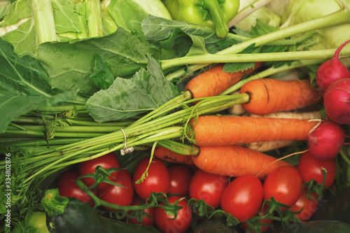 Carrots, tomatoes, radish, and green leaves mixed on display at fruit and vegetable market