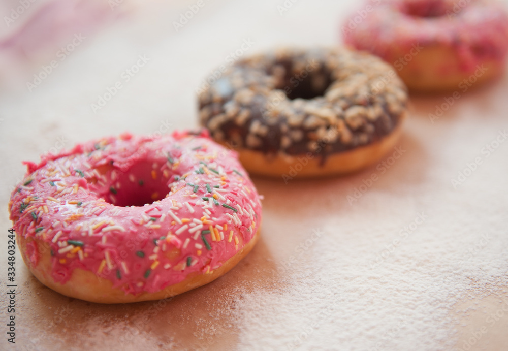 Three delicious doughnuts in pink and chocolate glaze are on a craft background, sprinkled with powdered sugar. Sweet food, fast food, obesity, pleasure Three delicious doughnuts in pink and chocolate glaze are on a craft background, sprinkled with powdered sugar. Sweet food, fast food, obesity, pleasure