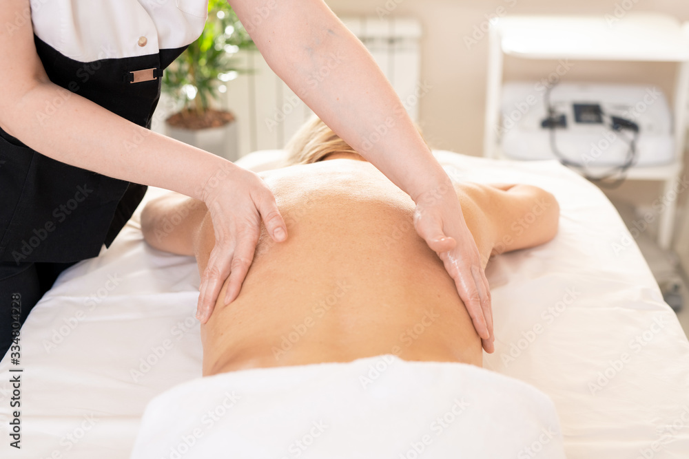 Unrecognizable therapist stroking back of woman while performing body massage at SPA procedure Unrecognizable therapist stroking back of woman while performing body massage at SPA procedure
