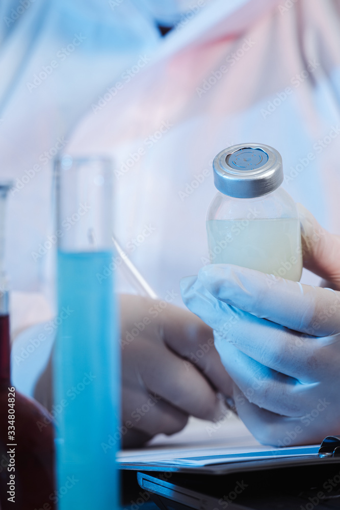 Fototapeta premium Glass medical bottle in a doctor's hand. A bottle with a medicine holds a hand in silicone gloves in a hospital. The nurse prepares the vaccine. A breakthrough in treatment. Antiviral vaccination.