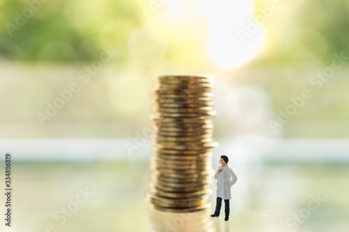 Healthcare,  Coronavirus (COVID-19) situation Business and Econony Cocept. Doctor miniature figure people with face mask standing with unstable stack of coins with copy space. photo