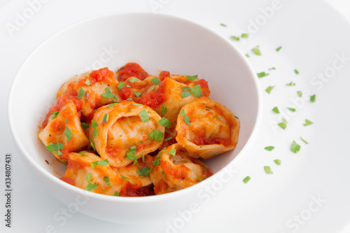 a bowl of ravioli with tomato sauce on a plate decorated with parsley