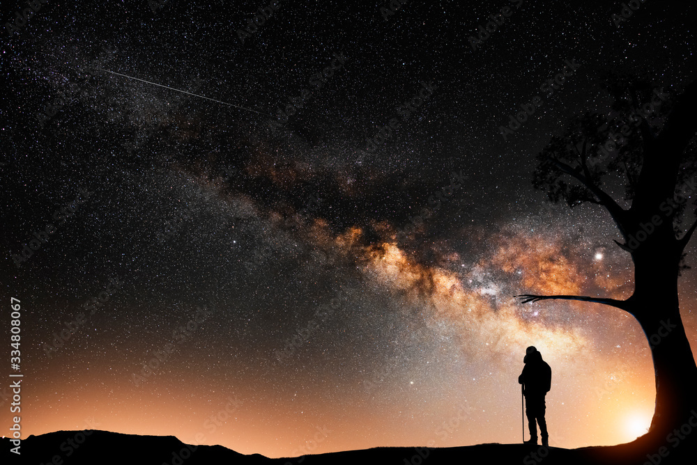Man silhouette stands on the hill, behind him beautiful bright milky way galxy on the night sky.  