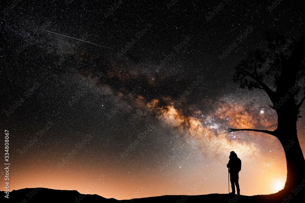 Fototapeta premium Man silhouette stands on the hill, behind him beautiful bright milky way galxy on the night sky. 