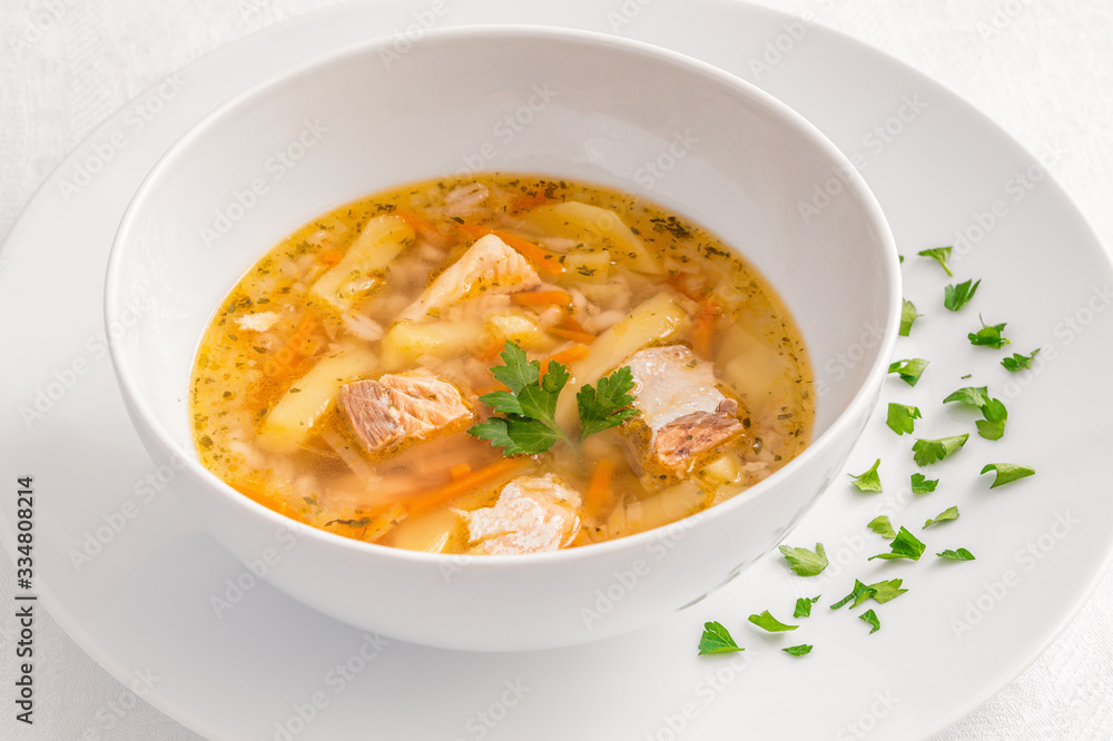 a bowl of salmon soup served on a plate decorated with parsley leaves