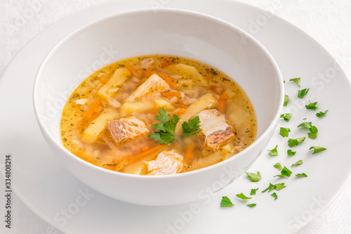 a bowl of salmon soup served on a plate decorated with parsley leaves