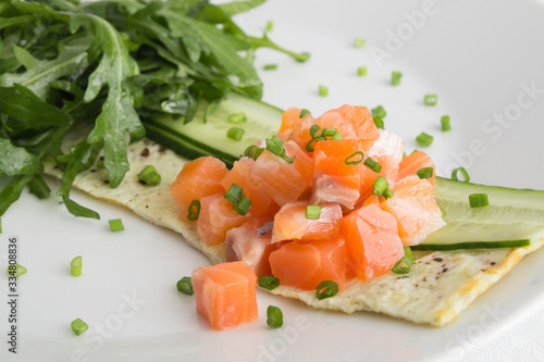 salmon chops on cucumber and thin omelette sprinkled with onion served with arugula leaves 