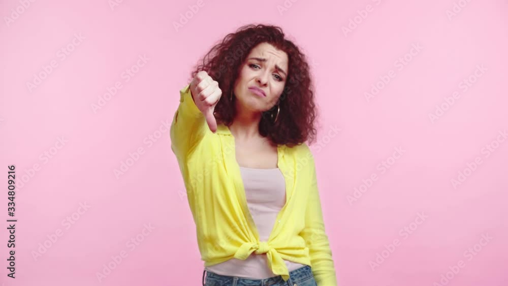 displeased girl showing thumb down while looking at camera isolated on pink displeased girl showing thumb down while looking at camera isolated on pink