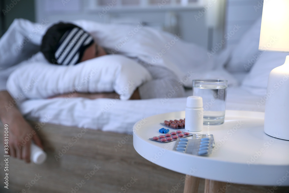 Pills for insomnia on table in bedroom of young man