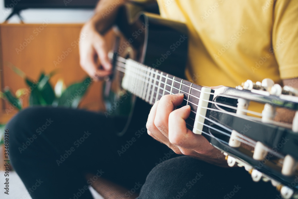 Close-up of a man hands holding and playing Acoustic Guitar at home with beautiful modern interior. Guitar player   practicing guitar scales. Selective focus, lifestyle photo