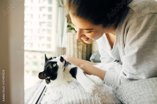Young woman playing with cute cat, sitting together at home during coronavirus quarantine. Stay home stay safe. Isolation at home to prevent virus epidemic. Hipster girl with cat in modern room