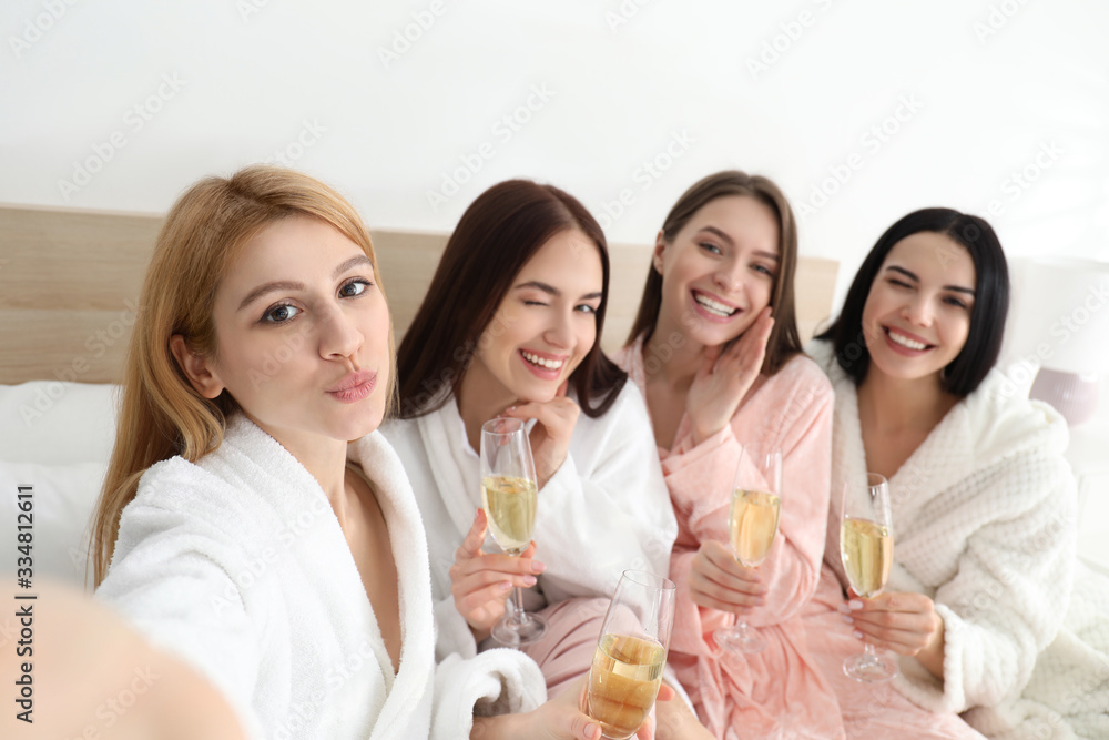 Beautiful young ladies with champagne taking selfie on bed at pamper party. Women's Day Beautiful young ladies with champagne taking selfie on bed at pamper party. Women's Day
