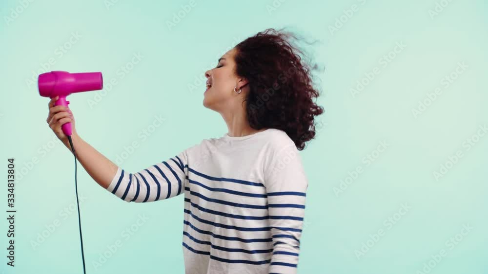 happy girl drying curly hair with hairdryer isolated on turquoise happy girl drying curly hair with hairdryer isolated on turquoise