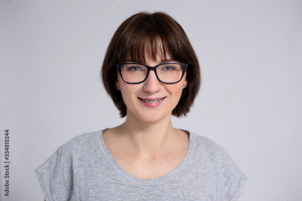 smiling woman in eyeglasses with braces on teeth over gray background