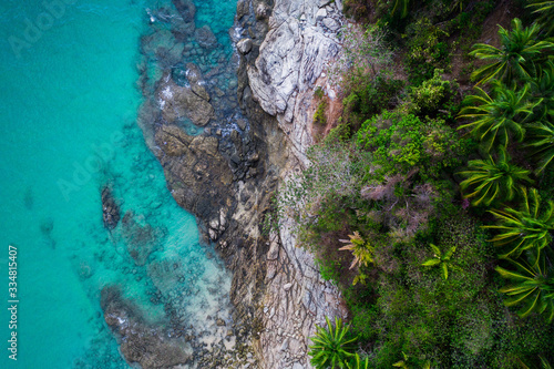 Aerial drone view of rocky shore with turquoise sea water and tropical green trees