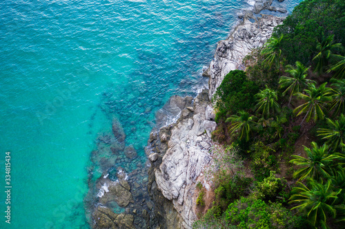 Aerial drone view of rocky shore with turquoise sea water and tropical green trees