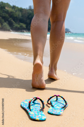 Girl rear view walking barefoot on the sand. Beach shoes in the foreground