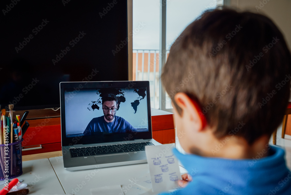 Boy studying homework during his online lesson at home, social distance during quarantine. Self-isolation and e-learning concept caused by coronavirus pandemia Boy studying homework during his online lesson at home, social distance during quarantine. Self-isolation and e-learning concept caused by coronavirus pandemia
