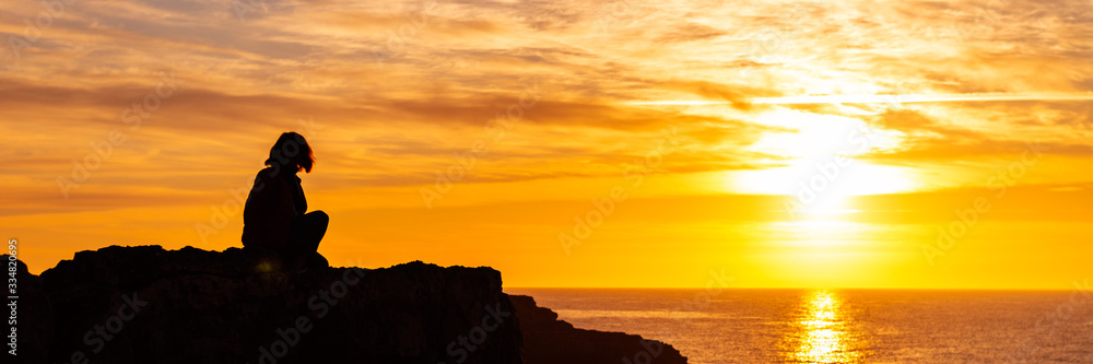 Silhouette of young woman on the edge of the cliff with sea view during sunrise. Holidays and enjoying life concept, banner size