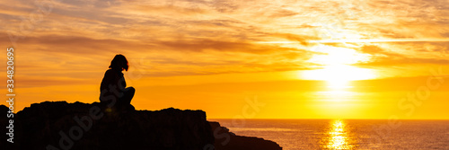 Silhouette of young woman on the edge of the cliff with sea view during sunrise. Holidays and enjoying life concept, banner size