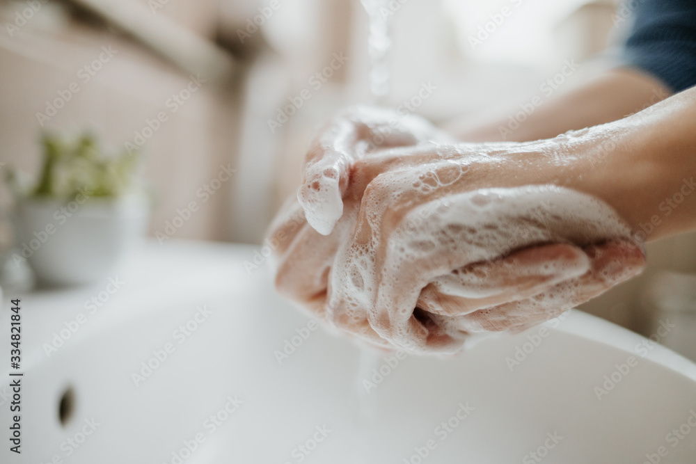 Fototapeta premium Closeup of a woman washing her hands in bathroom to prevent Covid-19 viral infection. Recommended washing with soap and running water during coronavirus pandemic.