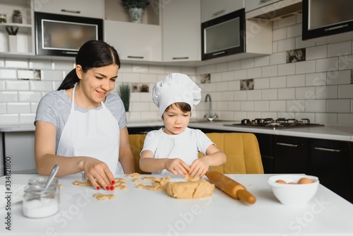 Little boy helping his mother with the baking in the kitchen standing at the counter alongside her kneading the dough for the pie