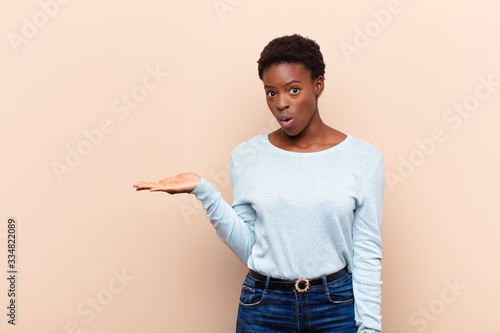 young pretty black womanlooking surprised and shocked, with jaw dropped holding an object with an open hand on the side photo