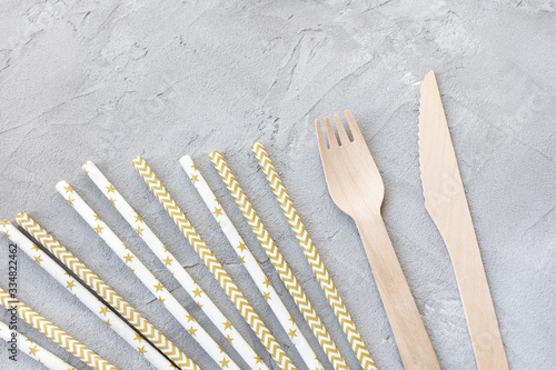 Disposable eco friendly trendy paper straws and wooden cutlery on gray background, knives and forks. Zero waste concept, recycling. Plastic-free alternative, environmental protection. Copy space