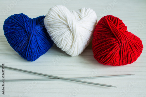 Three multicolored balls of wool in the shape of a heart: blue, red, white on a wooden table close-up and knitting needles. Concept: flag of France.