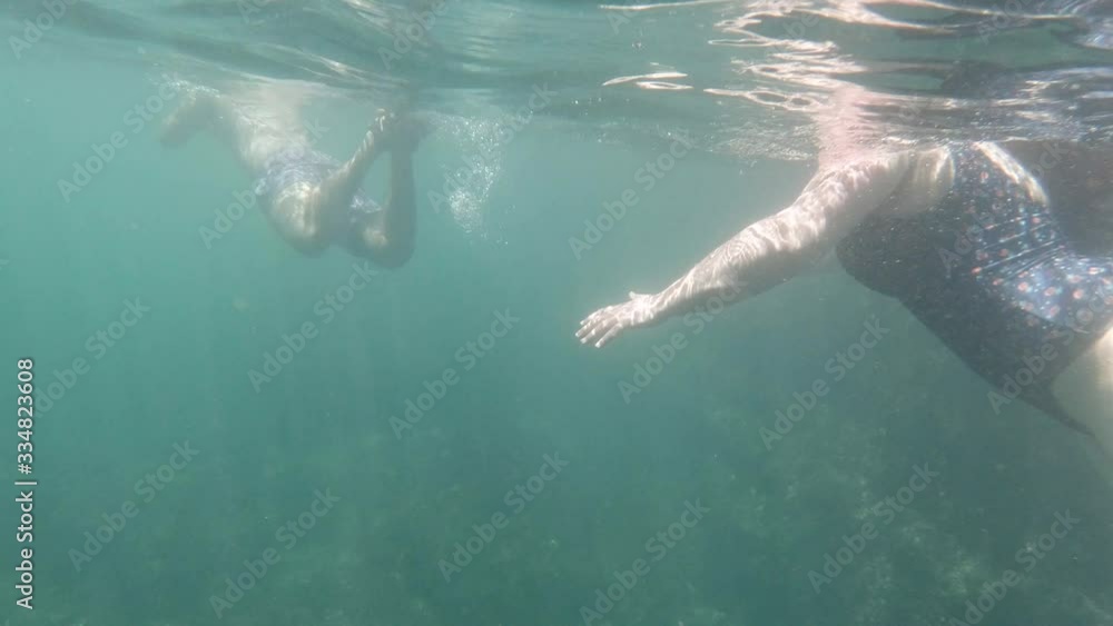 Slow motion underwater shot of body without face of a fat woman and a fit man swimming together inside the sea Slow motion underwater shot of body without face of a fat woman and a fit man swimming together inside the sea