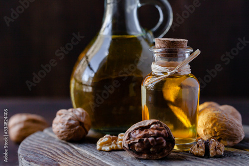 Concept of vegetable fat and oils for cooking and cosmetology. Glass bottle with essence, raw walnut peeled and in their shells. Wooden board, dark wooden background, close up, macro