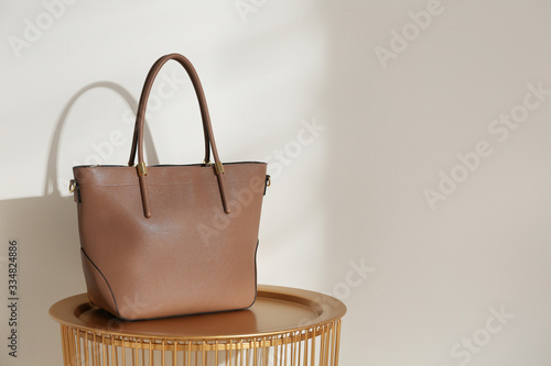 Stylish leather woman's bag on table near light wall. Space for text photo