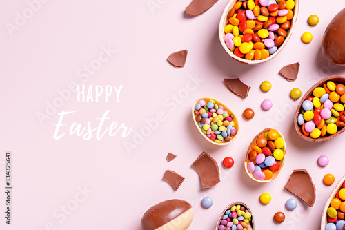 Happy Easter card with chocolate eggs and colorful candy sweets on pastel pink, copy space. Traditional Easter treats flat lay, holiday background