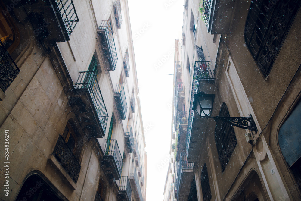 Bottom view of a dark narrow street on old historic houses with balconies and lanterns on a rainy winter day. Barcelona, Spain