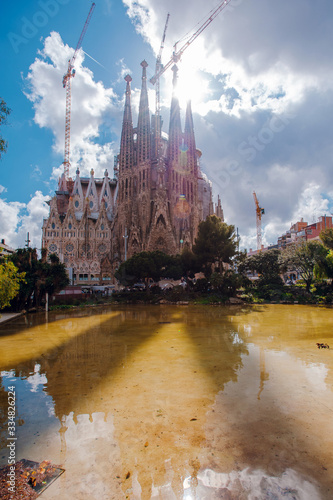 View of La Sagrada Familia, impressive cathedral in Barcelona, with a small lake and trees. Architecture and art, cultural heritage