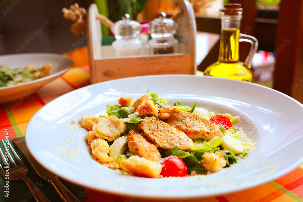 Caesar salad with croutons, quail eggs, cherry tomatoes and grilled chicken in a white plate on a table in a restaurant Caesar salad with croutons, quail eggs, cherry tomatoes and grilled chicken in a white plate on a table in a restaurant