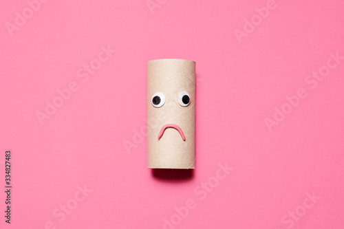 Sad frowning empty toilet paper roll with googly eyes and mouth on a pink background with room for text and copy space