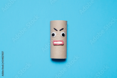 Angry empty toilet paper roll with googly eyes and mouth on a blue background with copy space and room for text