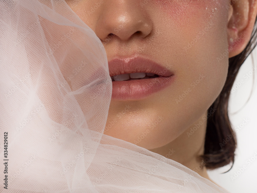Macro photo of female lips with beautiful skin and nude makeup. light transparent gloss on full lips and white flowers. Fashion photography. Cosmetology and spa. Freshness of spring Macro photo of female lips with beautiful skin and nude makeup. light transparent gloss on full lips and white flowers. Fashion photography. Cosmetology and spa. Freshness of spring