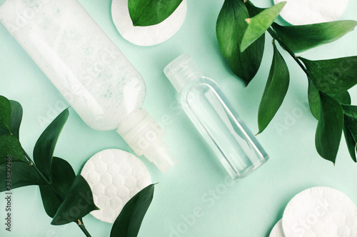 Beauty treatment products on pastel blue background with fresh green natural leaves, plastics bottle of facial toner top view, herbal skin care, eco hygiene.