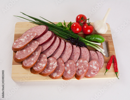 still life with sliced smoked sausage greens and tomatoes on a white background
