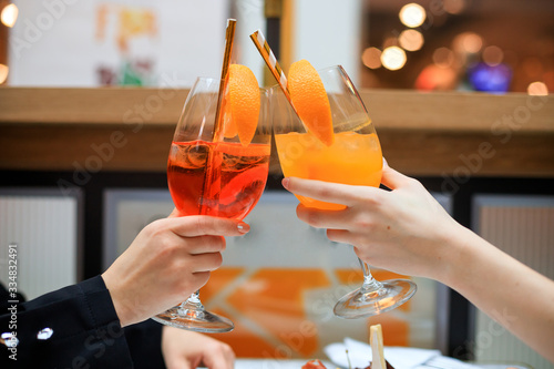 two girls drinking different aperol spritz in cafe. Woman hands raising glasses with colorful alcoholic drinks